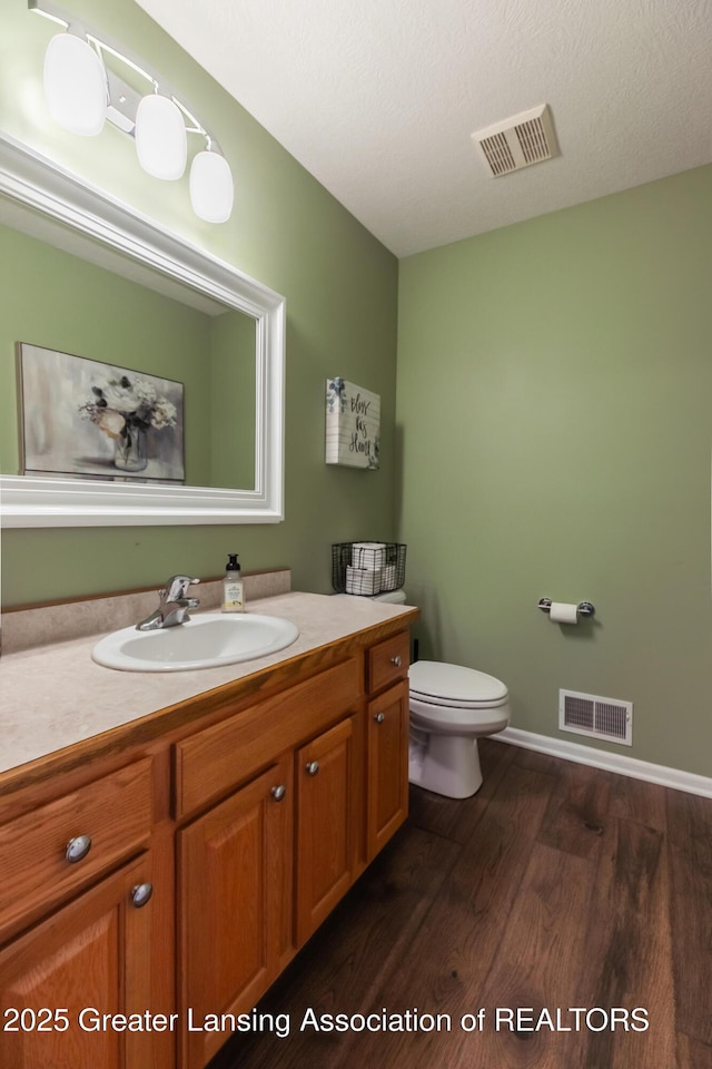 bathroom with toilet, visible vents, wood finished floors, and vanity