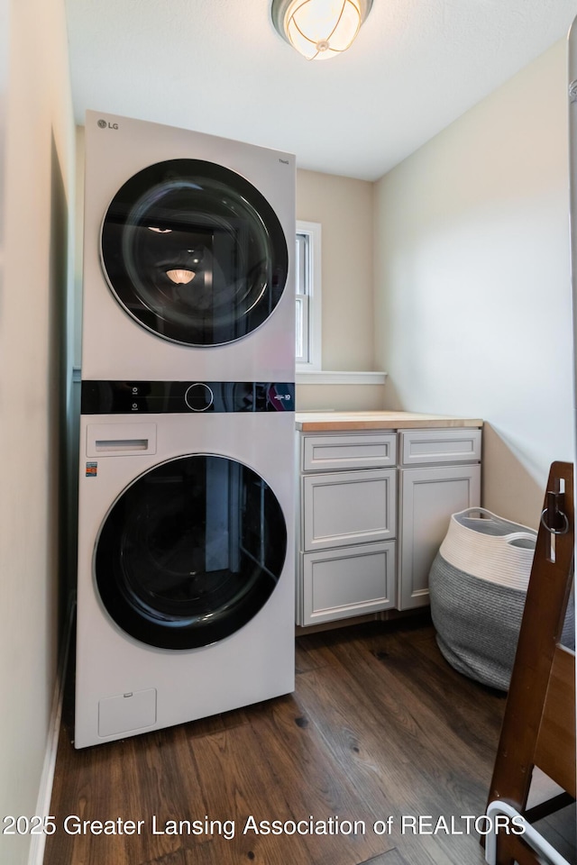 clothes washing area featuring dark wood finished floors, cabinet space, and stacked washer / drying machine