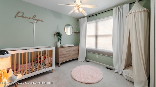 carpeted bedroom featuring ceiling fan, a crib, visible vents, and baseboards