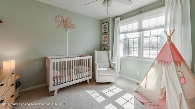 bedroom featuring a crib, carpet floors, baseboards, and a ceiling fan