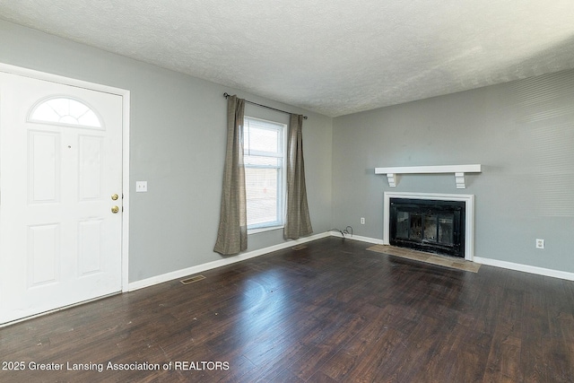 unfurnished living room with visible vents, a fireplace with flush hearth, a textured ceiling, and wood finished floors