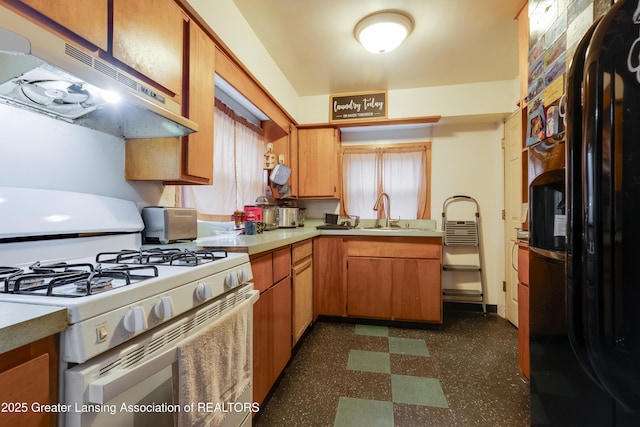 kitchen with dark floors, white gas range, freestanding refrigerator, a sink, and under cabinet range hood