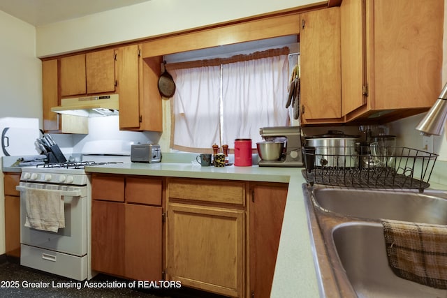 kitchen featuring light countertops, brown cabinetry, white gas range, and under cabinet range hood