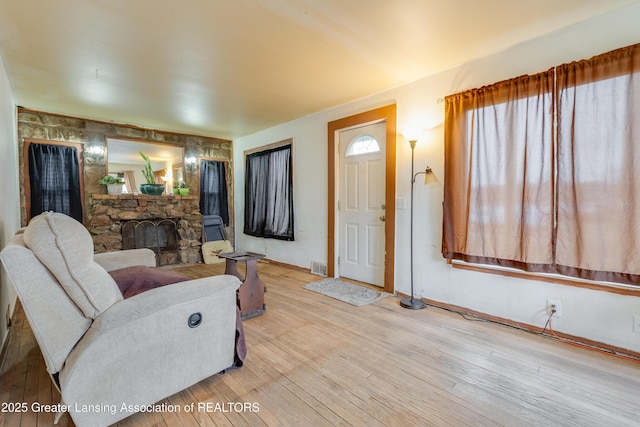 living room with wood-type flooring, a fireplace, visible vents, and baseboards