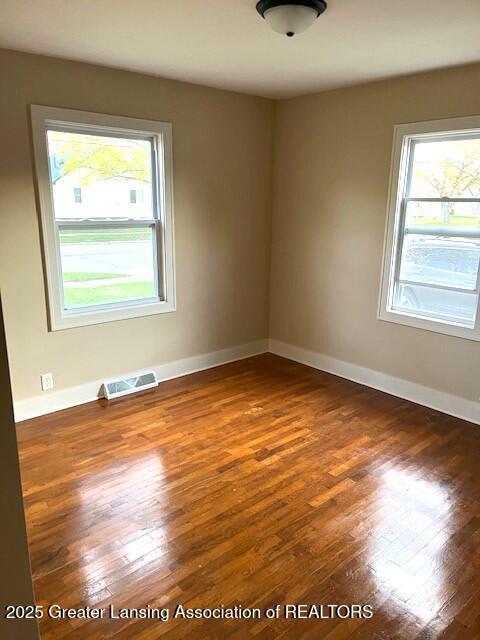 unfurnished room featuring visible vents, wood-type flooring, and baseboards