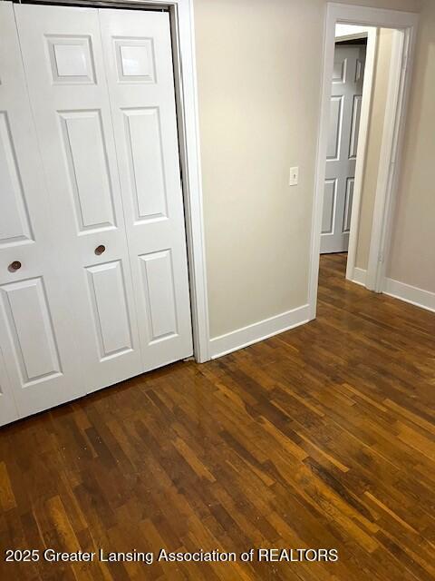 unfurnished bedroom with baseboards, dark wood-style floors, and a closet