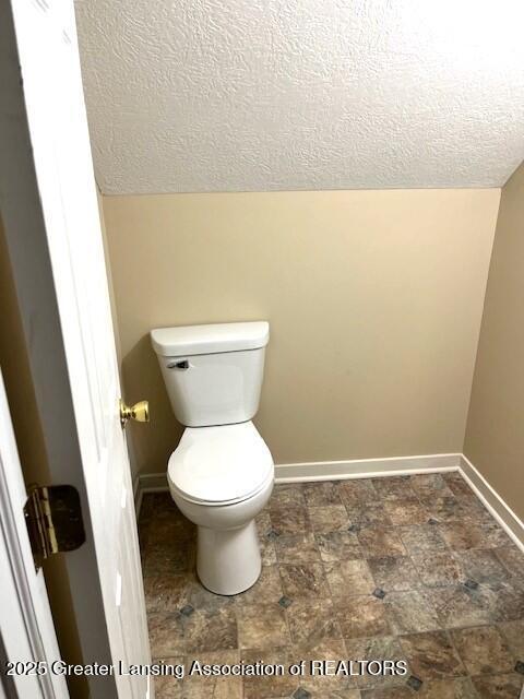 bathroom featuring baseboards, a textured ceiling, stone finish floor, and toilet