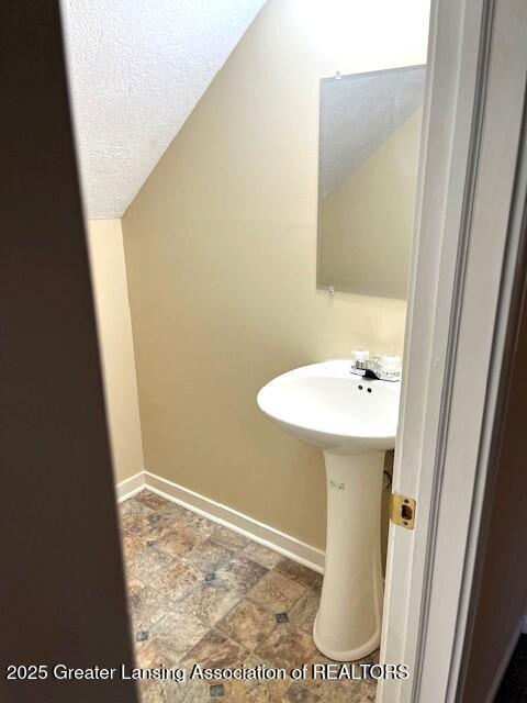 bathroom with baseboards, a sink, lofted ceiling, and stone finish floor