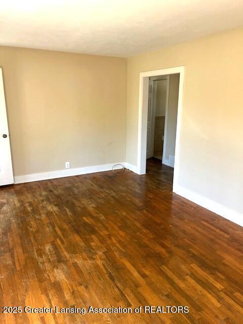 empty room with baseboards and dark wood-type flooring