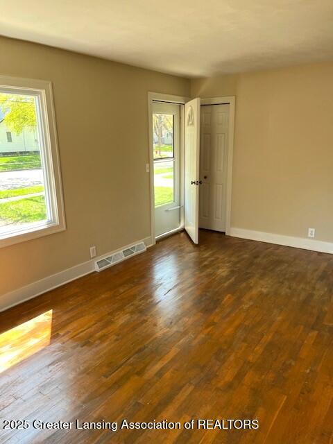 unfurnished room featuring baseboards, dark wood-type flooring, and visible vents