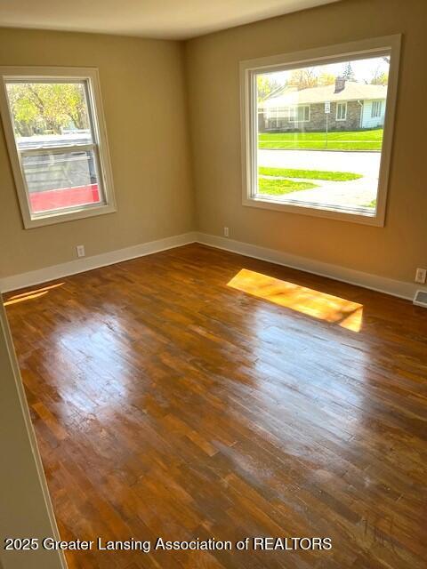 empty room featuring baseboards, dark wood finished floors, and a wealth of natural light