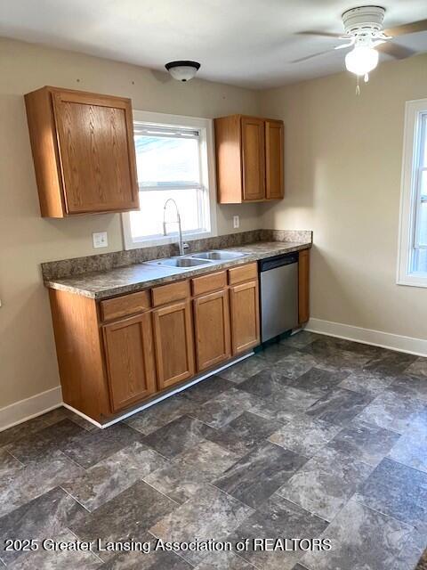 kitchen with a healthy amount of sunlight, brown cabinetry, stainless steel dishwasher, a sink, and baseboards