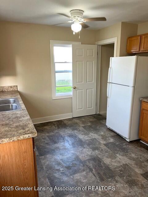 kitchen with ceiling fan, brown cabinetry, a sink, baseboards, and freestanding refrigerator