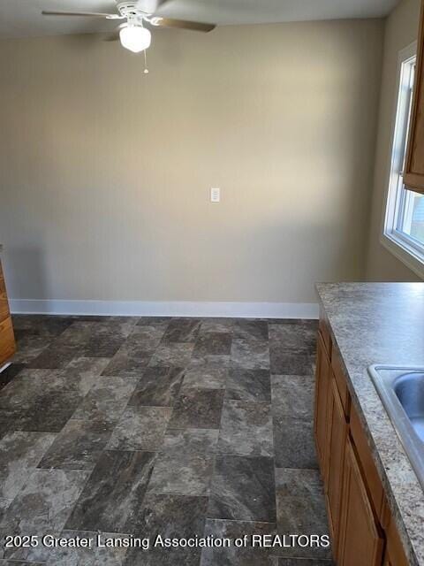unfurnished dining area with a sink, baseboards, ceiling fan, and stone finish floor