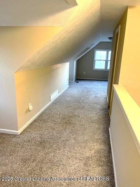 additional living space with visible vents, carpet, a textured ceiling, and lofted ceiling