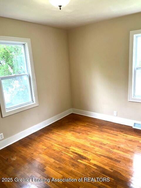 spare room with baseboards, plenty of natural light, and wood finished floors