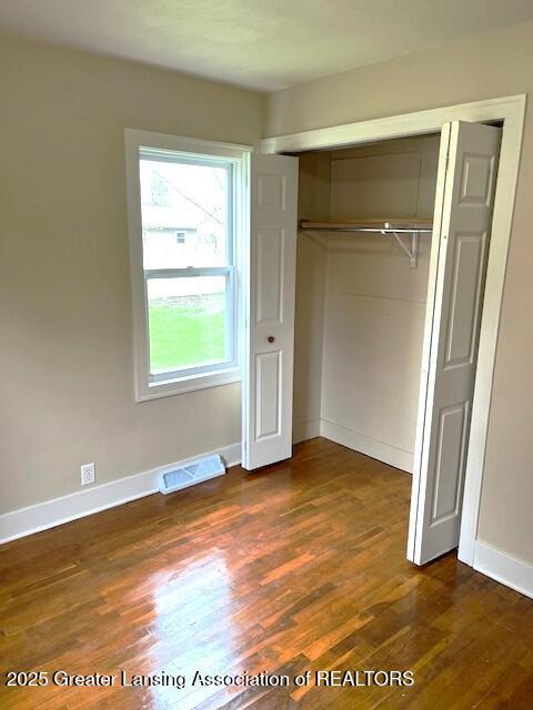 unfurnished bedroom featuring visible vents, baseboards, wood finished floors, and a closet
