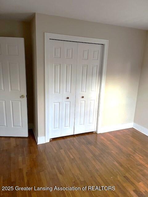 unfurnished bedroom featuring baseboards, a closet, and dark wood-type flooring