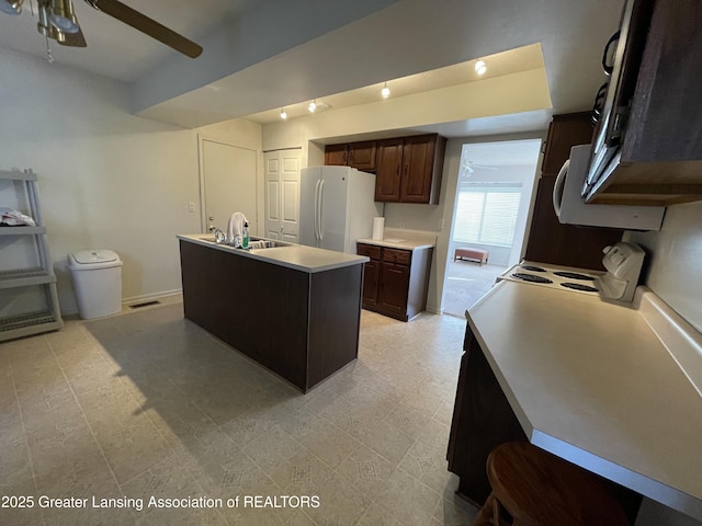 kitchen with white appliances, a center island with sink, a ceiling fan, light countertops, and a sink