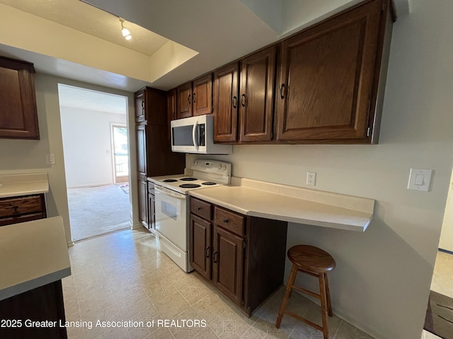 kitchen with dark brown cabinetry, a tray ceiling, light countertops, light floors, and white range with electric cooktop