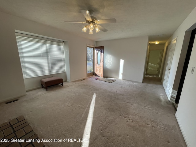 interior space featuring baseboards, a textured ceiling, visible vents, and a ceiling fan