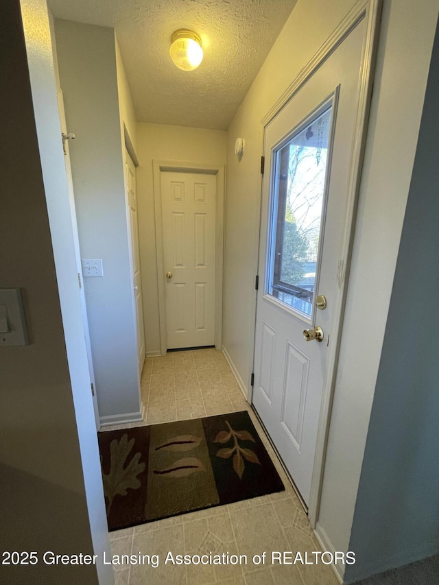 doorway to outside featuring baseboards and a textured ceiling