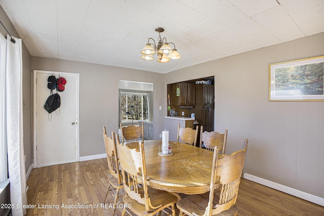 dining room featuring light wood-type flooring, a notable chandelier, and baseboards