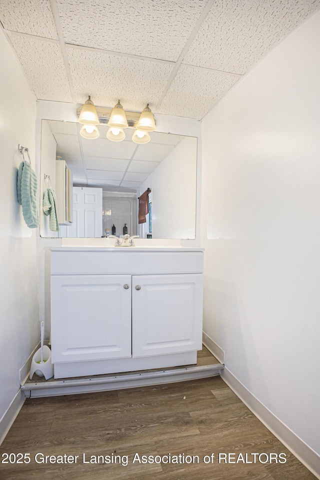 bathroom with a drop ceiling, wood finished floors, vanity, and baseboards