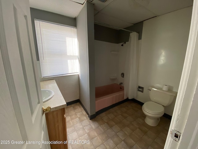 bathroom featuring baseboards, a drop ceiling, toilet, shower / tub combo, and vanity