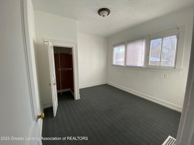 unfurnished bedroom with a closet, baseboards, a textured ceiling, and dark carpet