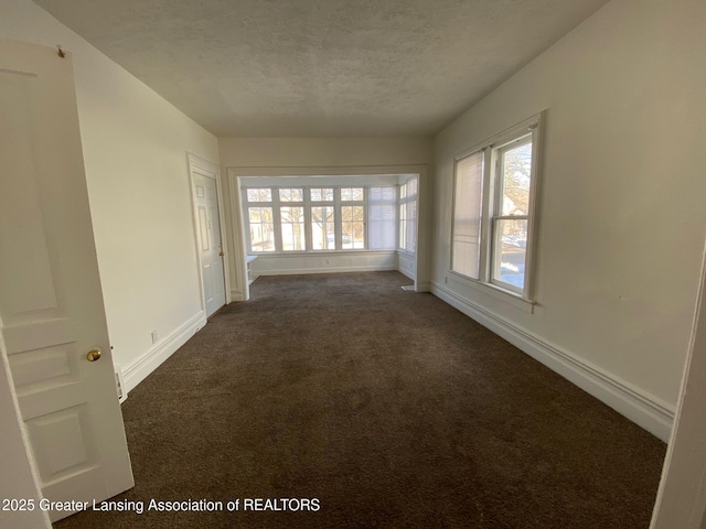 unfurnished room featuring a textured ceiling, baseboards, and dark colored carpet