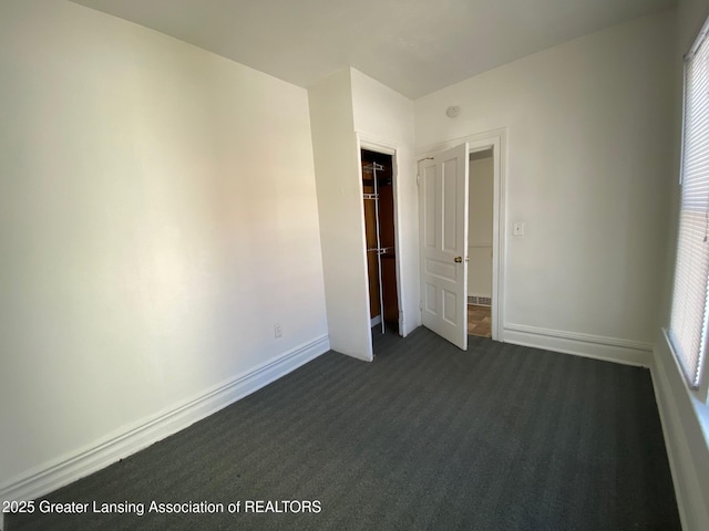 unfurnished bedroom with dark colored carpet and baseboards