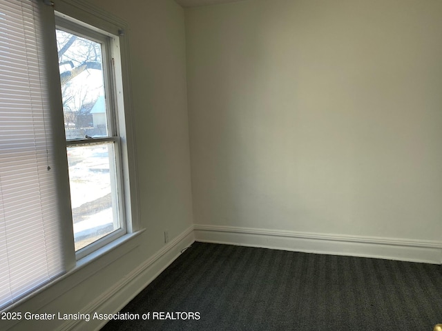 spare room featuring dark colored carpet and baseboards