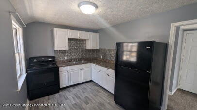 kitchen with lofted ceiling, decorative backsplash, black appliances, a textured ceiling, and white cabinetry