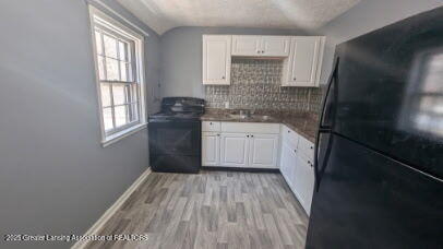 kitchen with white cabinets, black appliances, lofted ceiling, and a sink