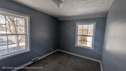 empty room with visible vents, baseboards, a textured ceiling, and dark carpet