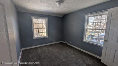 empty room featuring baseboards, a textured ceiling, and dark carpet