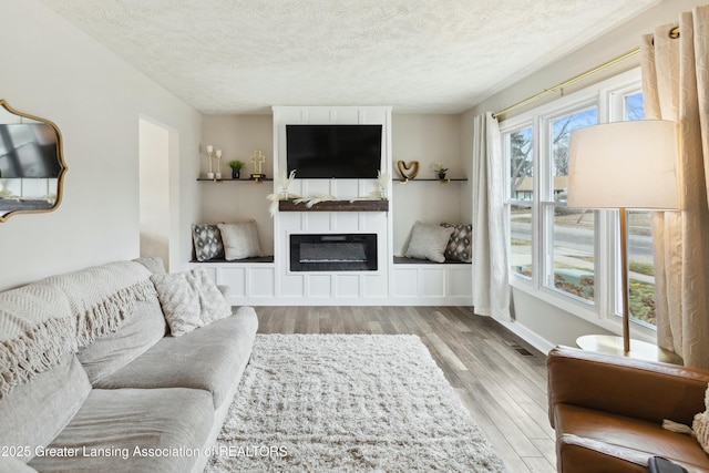 living room featuring a glass covered fireplace, wood finished floors, baseboards, and a textured ceiling