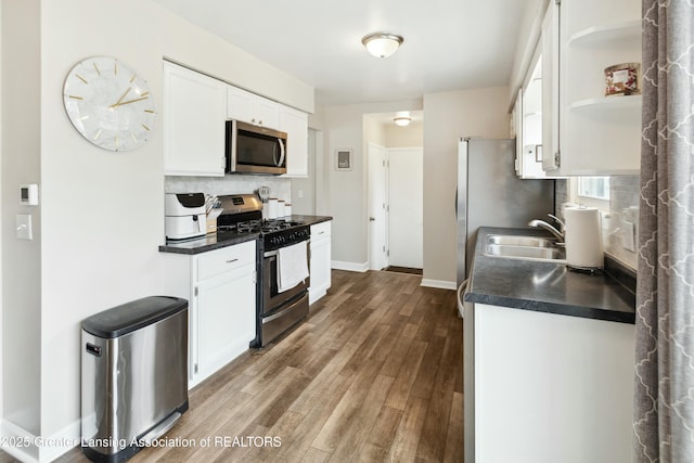 kitchen with open shelves, a sink, backsplash, dark countertops, and appliances with stainless steel finishes