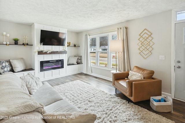 living room featuring a glass covered fireplace, a textured ceiling, baseboards, and wood finished floors