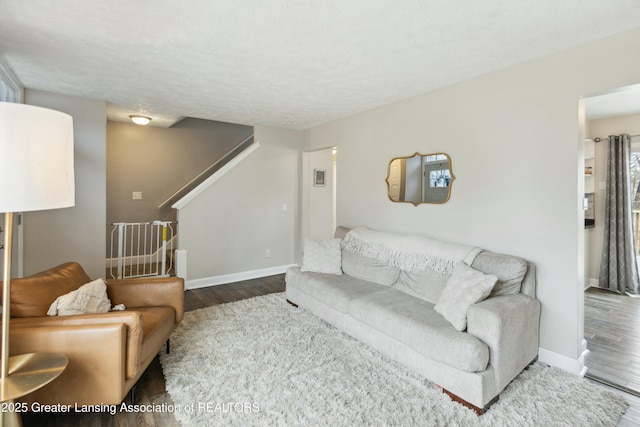 living area with stairway, baseboards, a textured ceiling, and wood finished floors