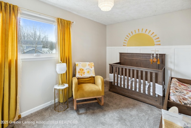 carpeted bedroom featuring a crib, wainscoting, and a textured ceiling