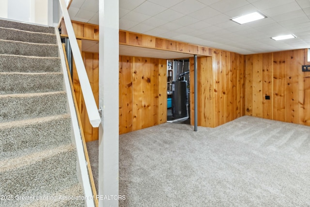 finished basement featuring stairway, a paneled ceiling, wood walls, and carpet floors