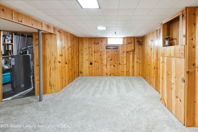 basement featuring carpet, water heater, and wood walls