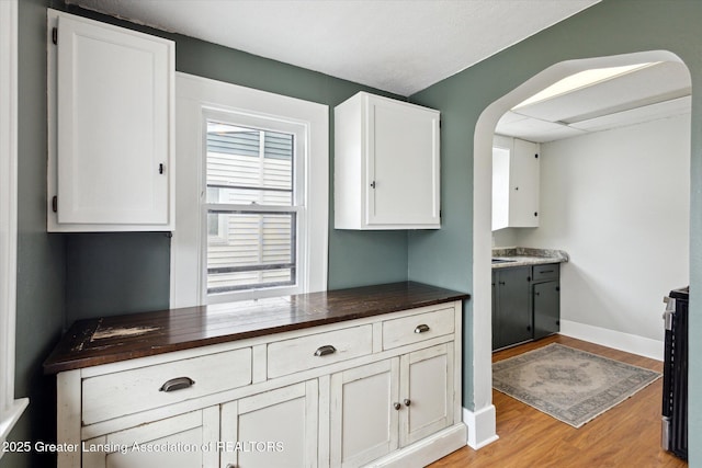 kitchen with baseboards, light wood finished floors, arched walkways, and white cabinetry