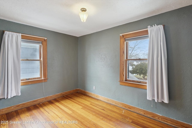 spare room with hardwood / wood-style flooring, a textured wall, and baseboards