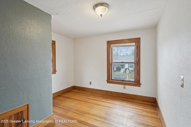 unfurnished room featuring a textured wall, baseboards, and light wood finished floors