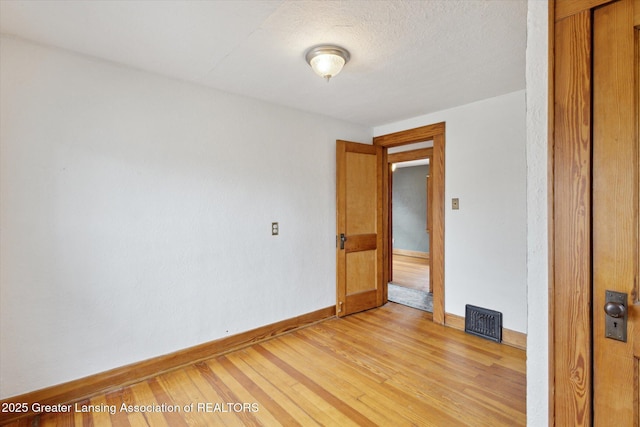 empty room featuring visible vents, baseboards, a textured ceiling, and light wood-style flooring