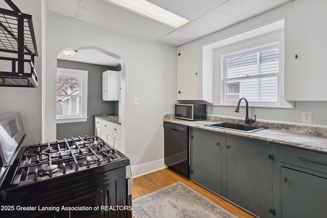 kitchen with gas range, dishwasher, light wood-type flooring, arched walkways, and a sink