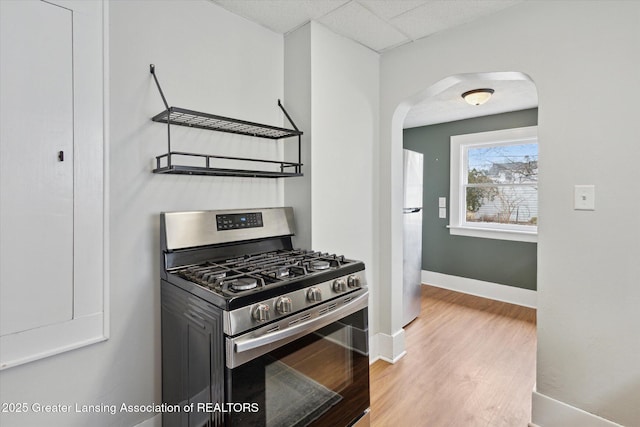 kitchen with wood finished floors, baseboards, arched walkways, a drop ceiling, and appliances with stainless steel finishes